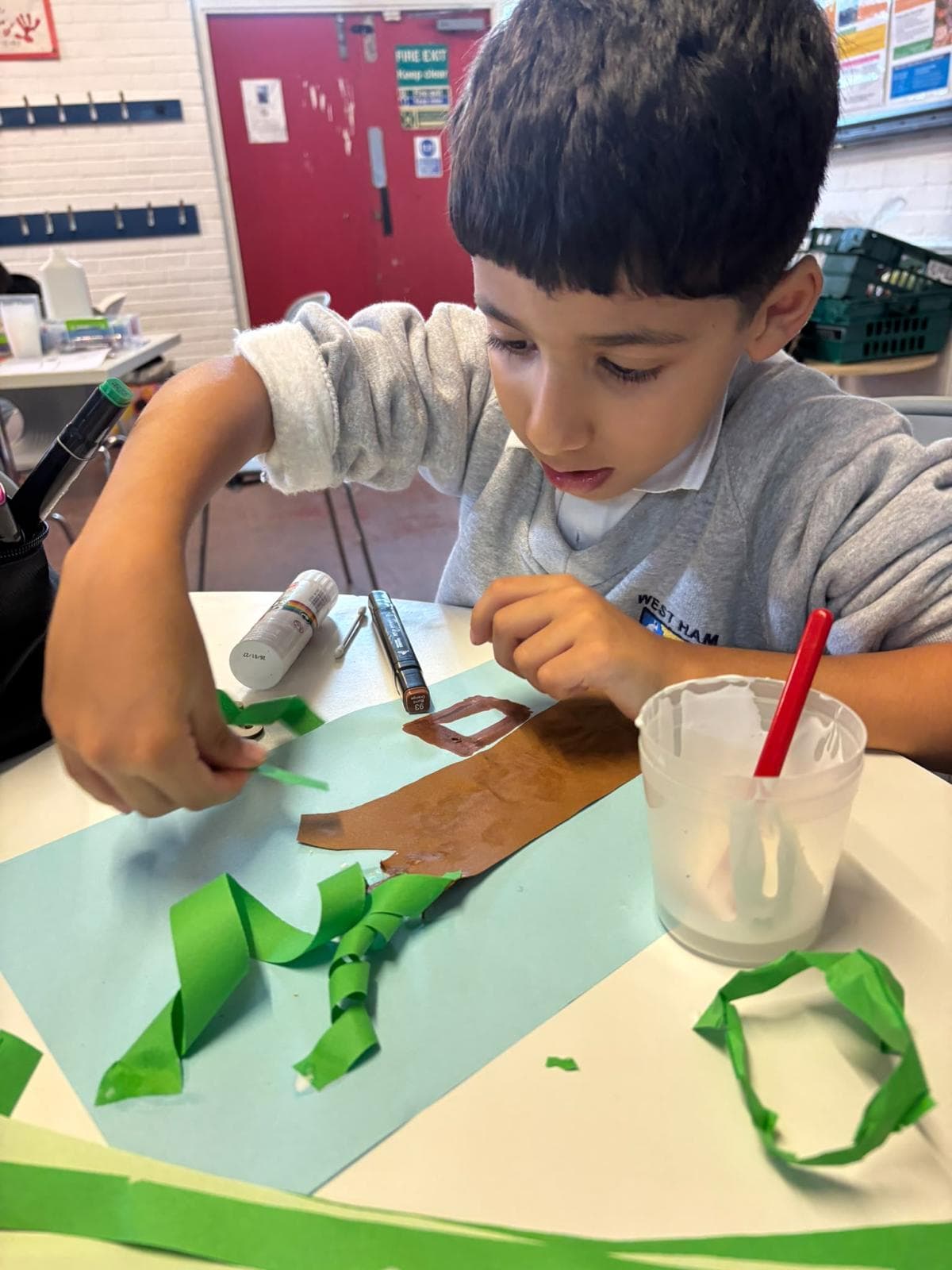 A young member gluing paper leaves onto a tree craft during an Arts & Craft session