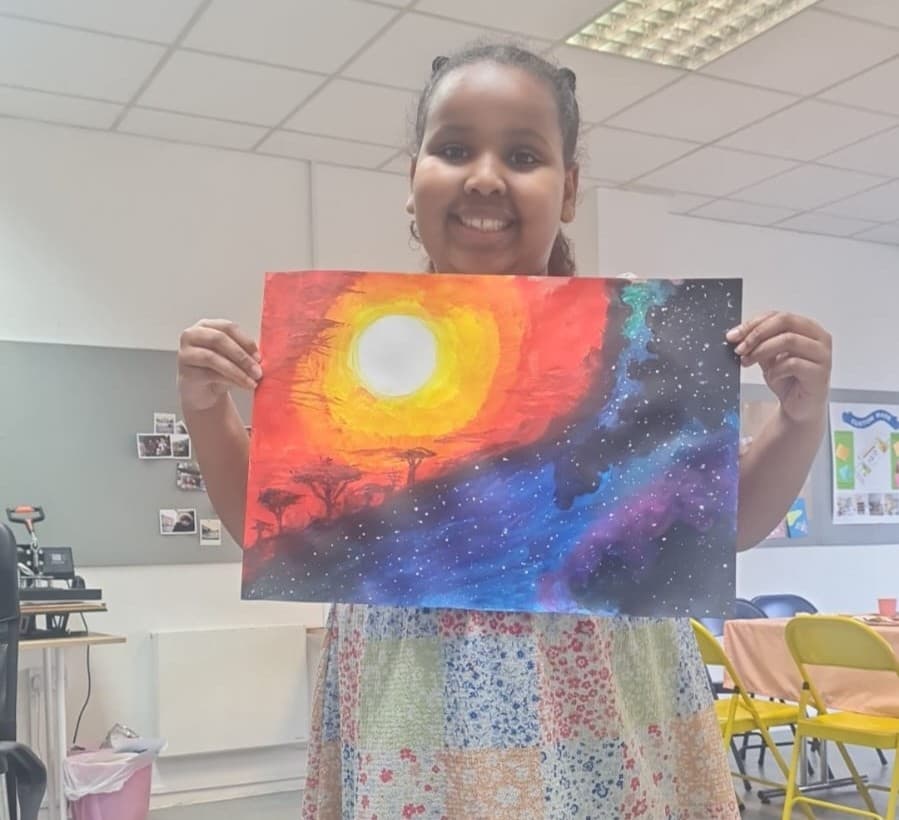 A young member proudly holding up their finished artwork